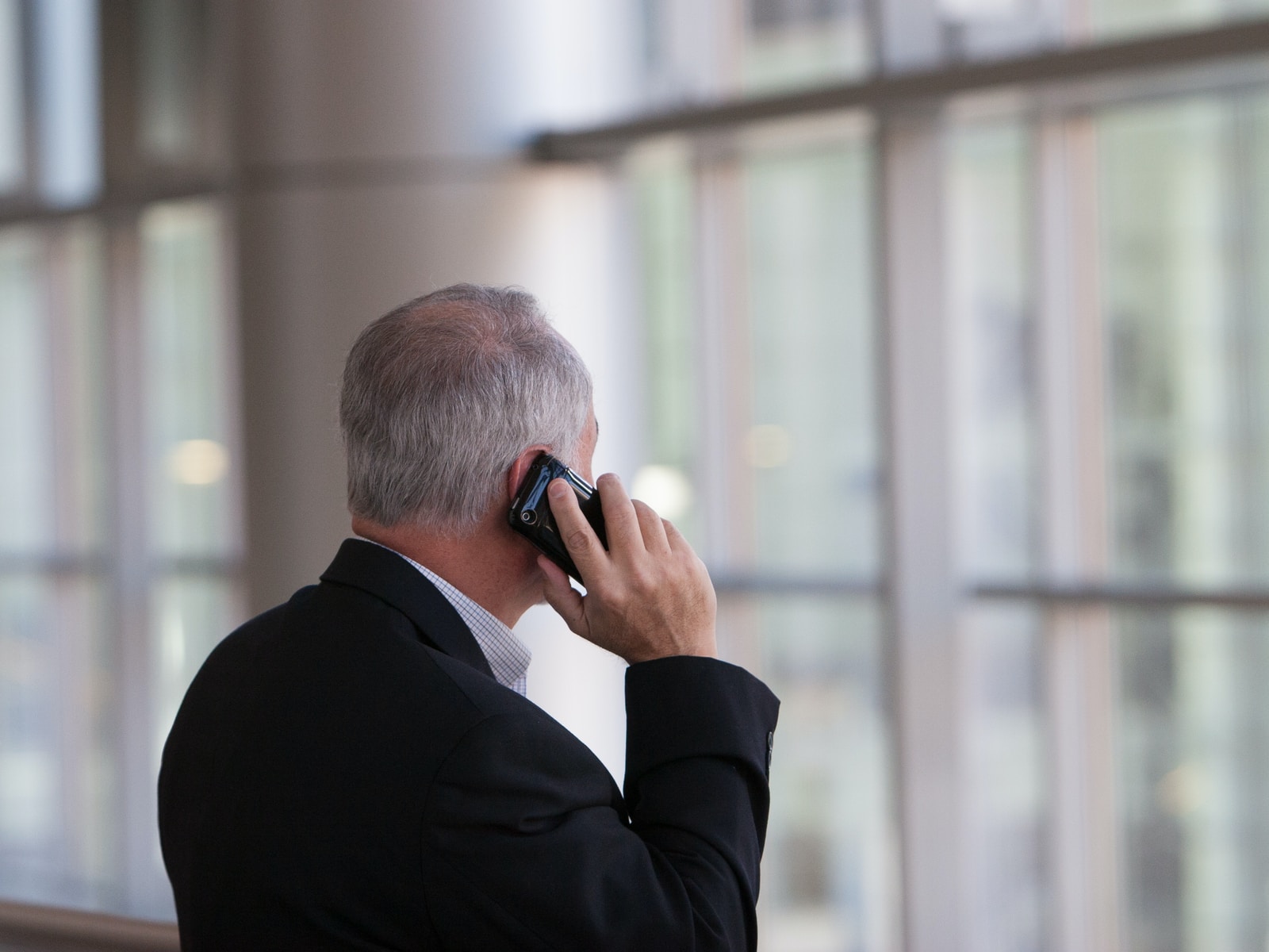 man holding black smartphone in front of a windowpane business phone system